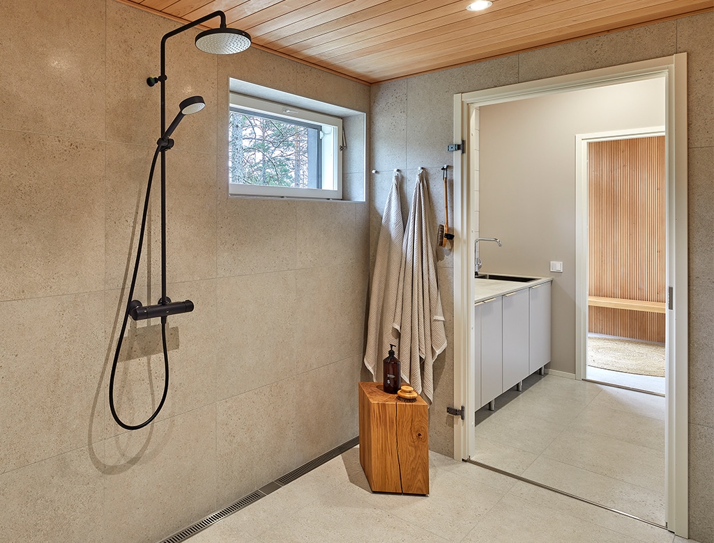 Kodin puukattoiselle saunaosastolle on valittu lämpimän hiekan sävyjä, ja pesuhuoneen lattialle valkoiset sekä seinille beigen väriset suuret neliölaatat.