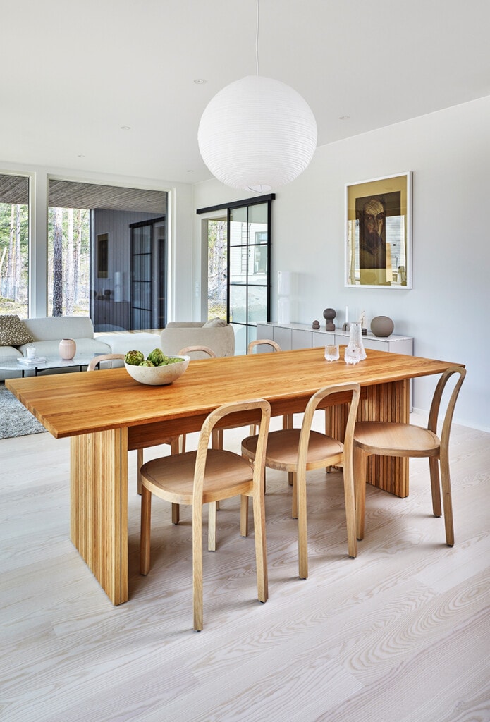 Puinen design-ruokailuryhmä luo pehmeän kontrastin puukuvioisen vaalean lattian kanssa Kastellin sisustussuunnittelijan sisustamassa omakotitalossa.