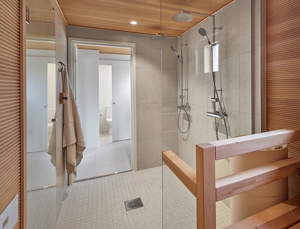 Pesuhuoneen seinät on kaakeloitu hiekanvärisillä suurilla neliölaatoilla. Saunassa on vaakasuuntaan asennetut sormipaneelit.
